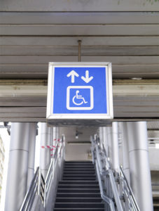 Fotografía de señalización en el transporte público que indica acceso a personas con discapacidad. Detrás de la señal, unas escaleras.