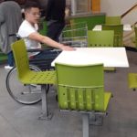 Fotografía de un usuario de silla de ruedas probando la altura de las mesas para la evaluación de accesibilidad en la zona de comida