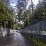 Fotografía de carretera de acceso a Reserva Santa Fe donde a los costados se pueden apreciar grandes árboles y una barda con una tela que da la bienvenida a la Reserva