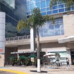 Fotografía del edificio Schneider National Sede México Vista frontal donde se puede apreciar un Café Starbucks, dos pequeña palmera y el edificio en general