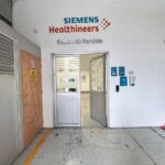 Fotografía de la puerta de acceso a zona de oficinas. Con una pared blanca y el texto de SIEMENS Healthineers pintado en la parte superior de la pared.