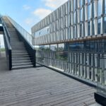Escaleras panorámica lateral al edificio con paredes de cristal y piso de madera.