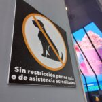 Señalización en la pared que indica que no hay restricción para perros guía o de asistencia acreditados, con un símbolo de prohibición sobre una silueta de perro y un fondo negro.