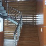 Escaleras y pared en acabado en madera con un barandal de metal
