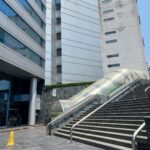 Entrada principal por medio de escaleras de cemento con pasamanos, que conducen a la plaza. Junto a las escaleras un túnel de acrílico.